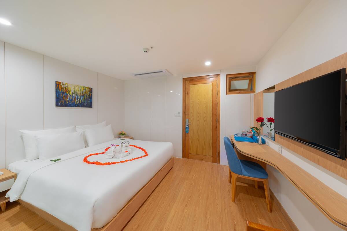 A hotel room with a bed, a desk, a chair, a flat-screen TV, and a wooden door.