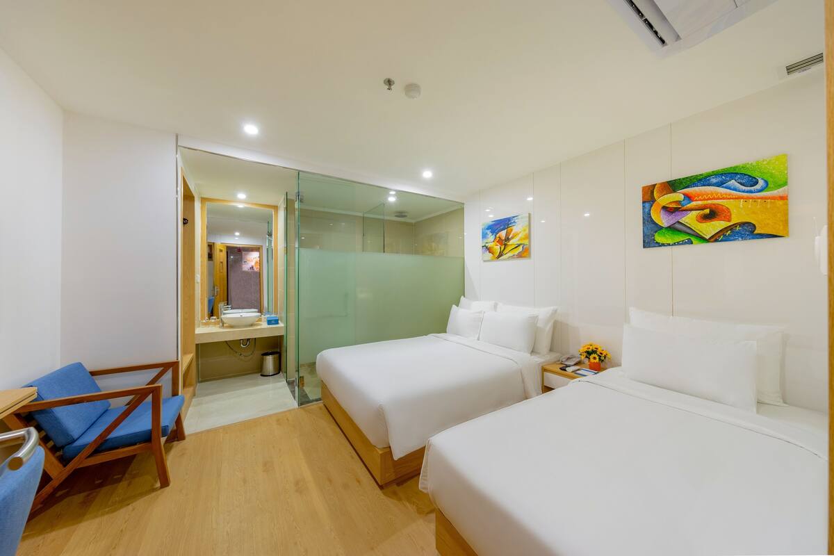 A hotel room with two beds, a small desk, a chair, a mirror, and a painting on the wall.