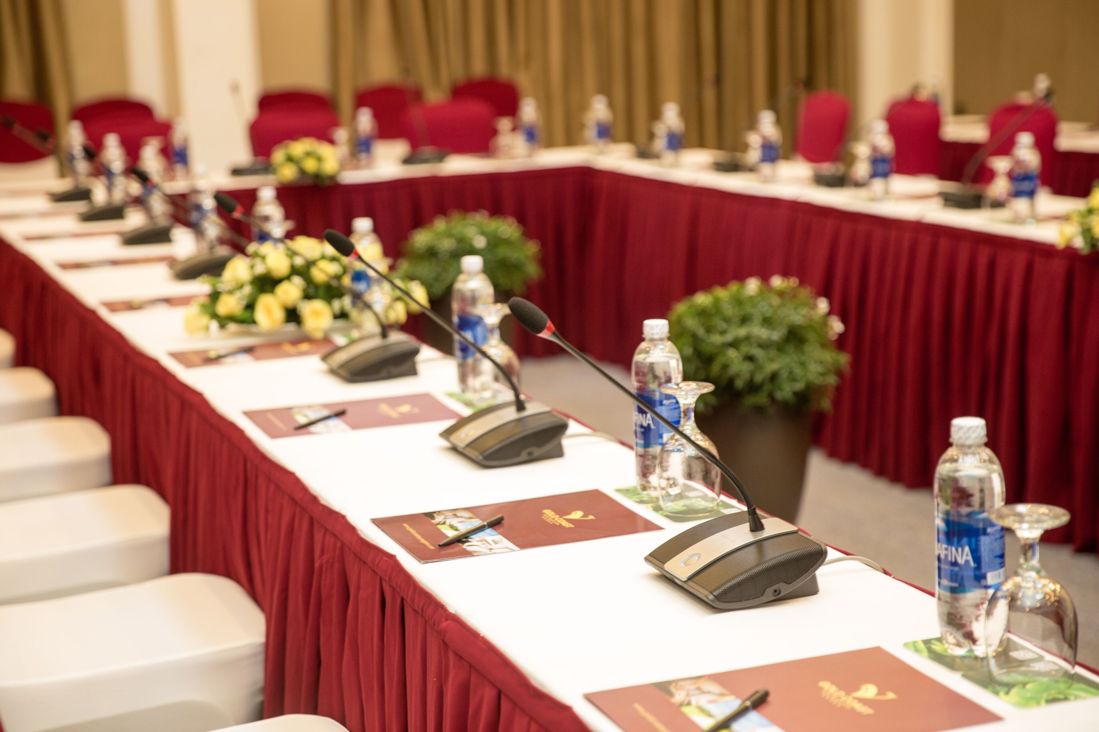 A conference room with a long table, microphones, nameplates, and water bottles.