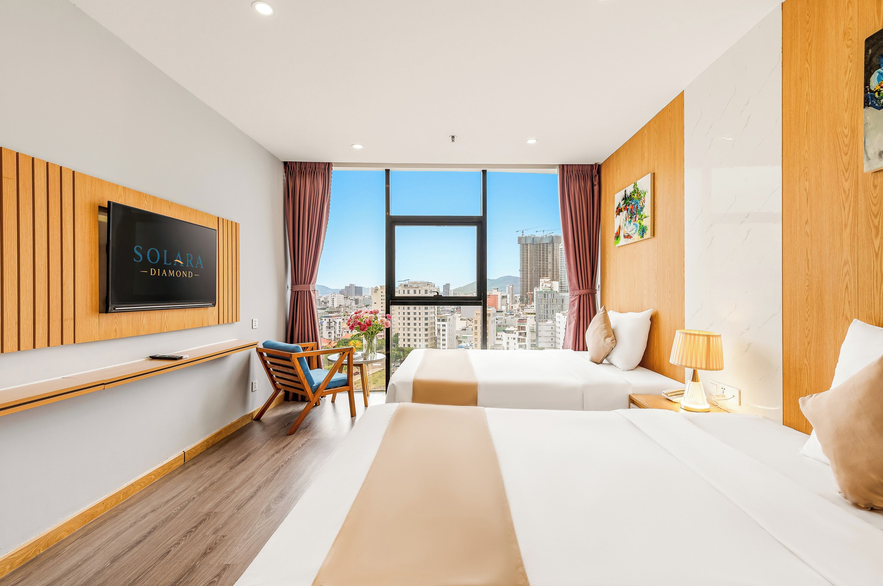 A hotel room with a bed, a desk, a chair, a TV, and a view of the city.