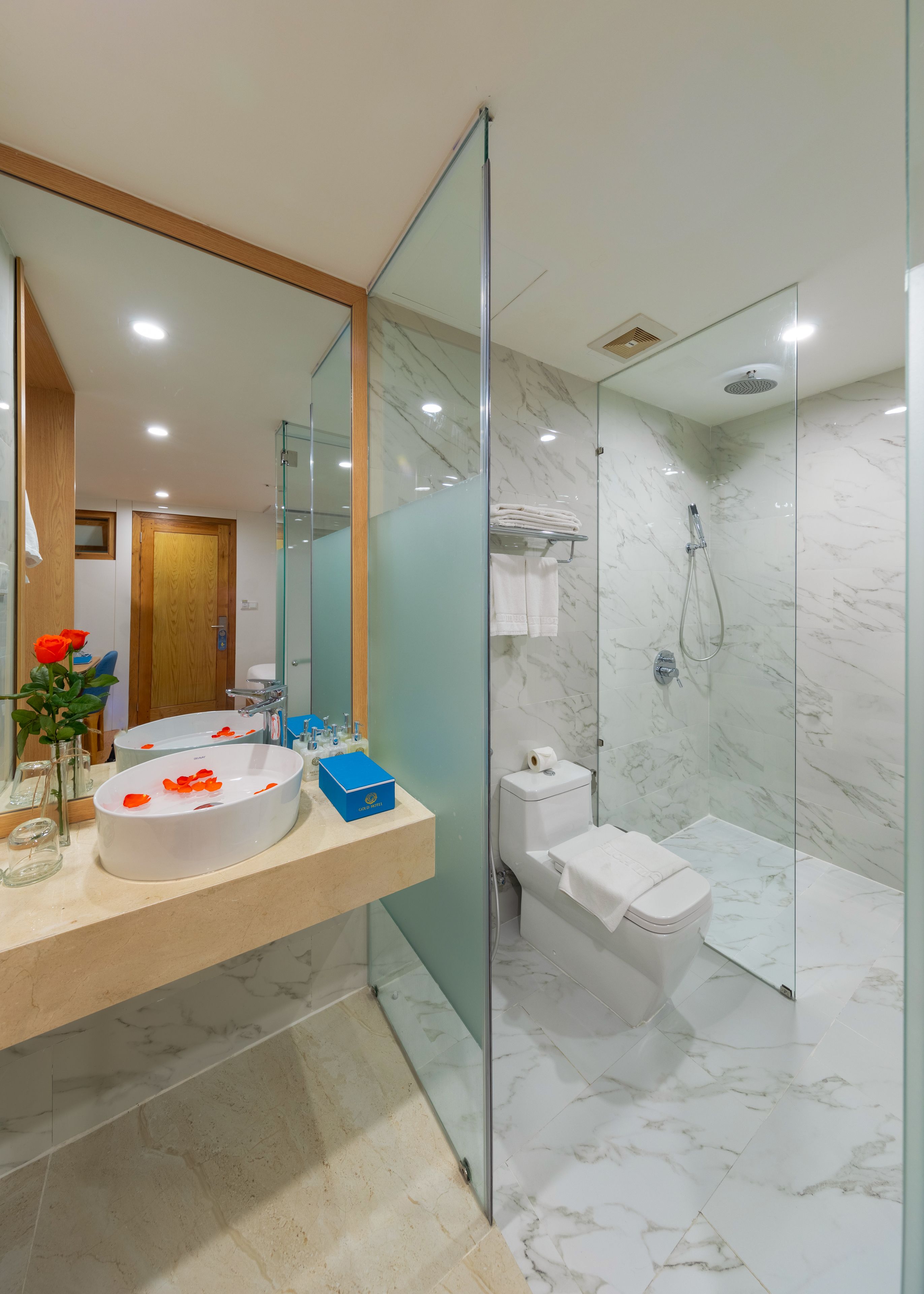A modern bathroom with a glass-enclosed shower, a marble-tiled floor, and a large mirror above the sink.