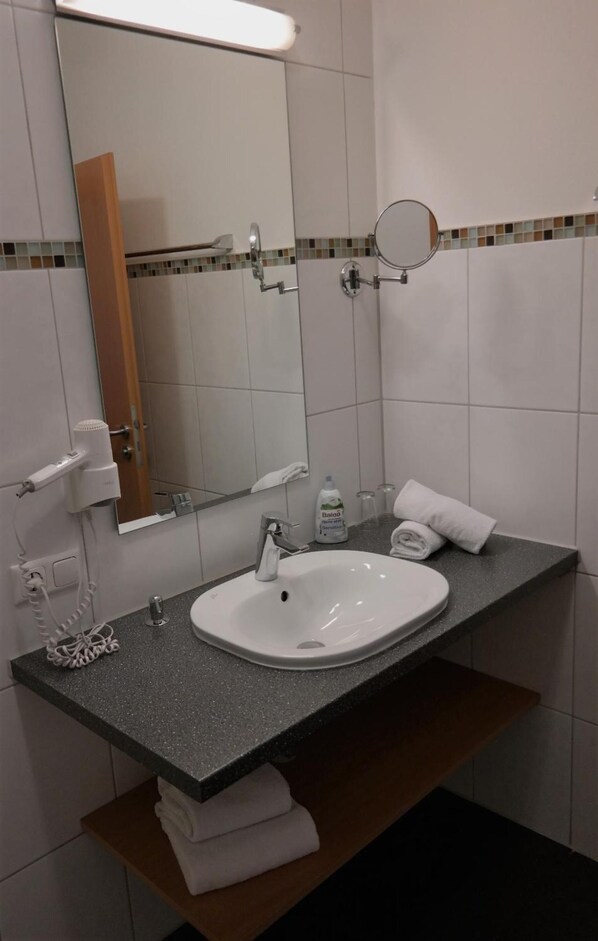 Un baño con lavamanos blanco, espejo, toallero y jabón para manos.
