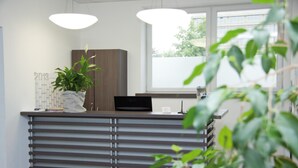 Un mostrador de recepción con una planta en maceta, un calendario y un monitor de computadora.