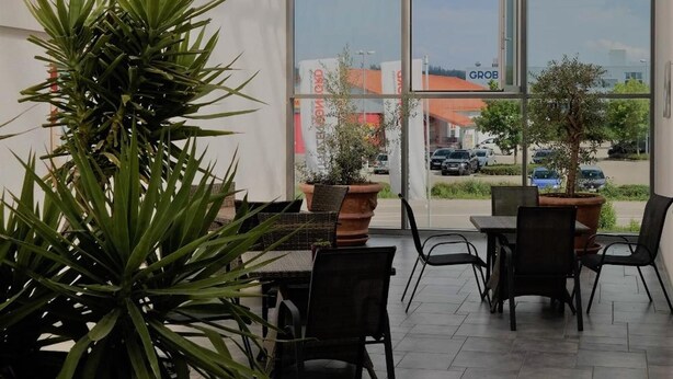 Un patio interior con amplios ventanales, plantas en macetas y mobiliario de exterior.
