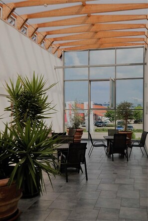 Un patio interior con amplios ventanales, plantas en macetas y mobiliario de exterior.