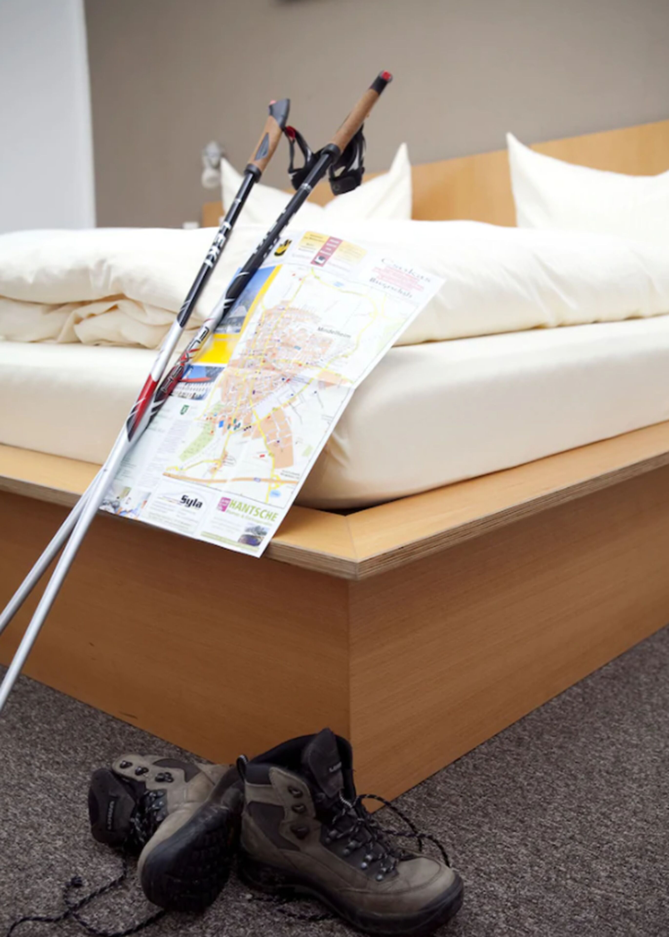 A bed with a map and trekking poles leaning against it.
