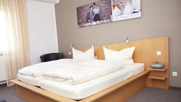A modern hotel room with a wooden bed, a bedside table, and a wall-mounted shelf.
