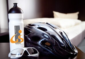 Un casco de bicicleta negro, una botella de agua blanca y unas gafas de sol blancas sobre una superficie de madera.