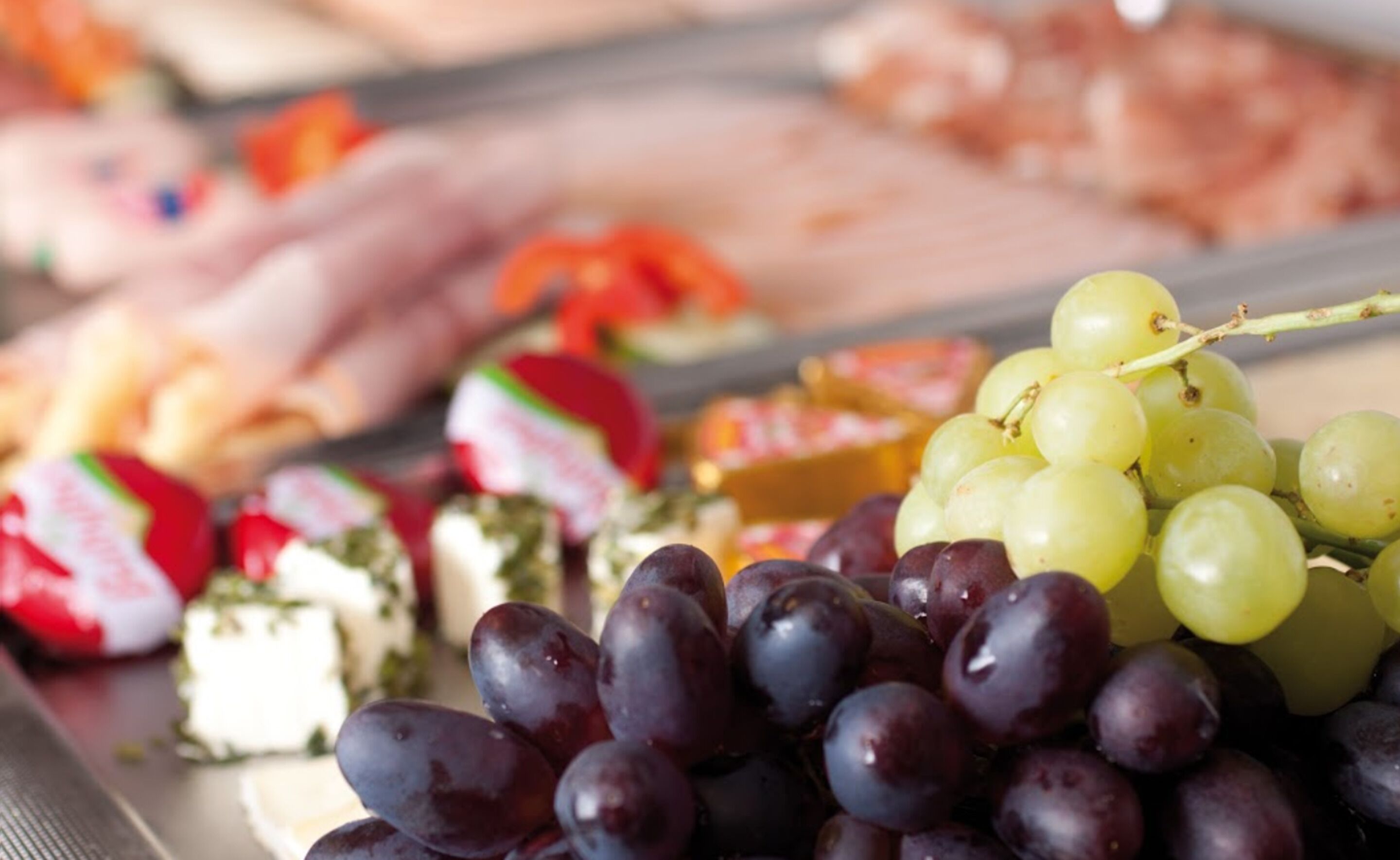 A variety of food items including grapes, cheese, and cured meats on a tray.