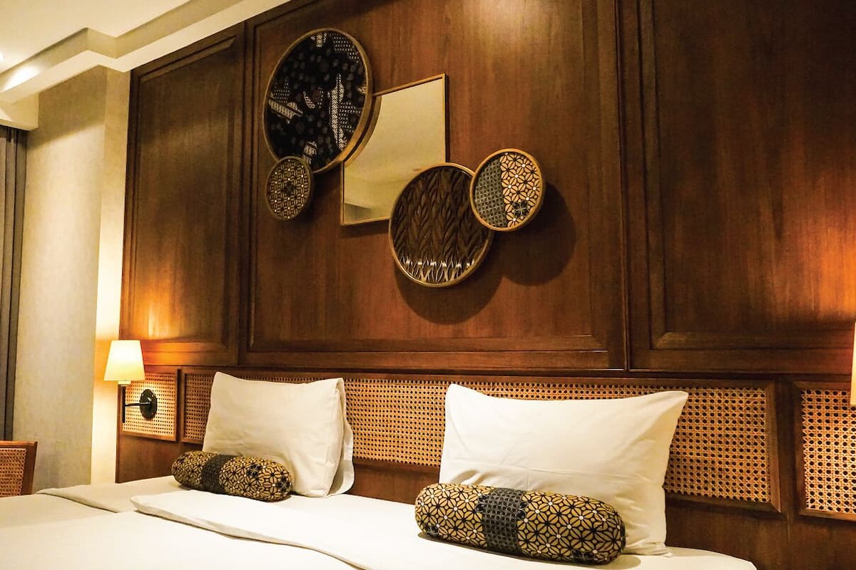A hotel room with a wooden headboard, a bed with white linens, and decorative wall mirrors.