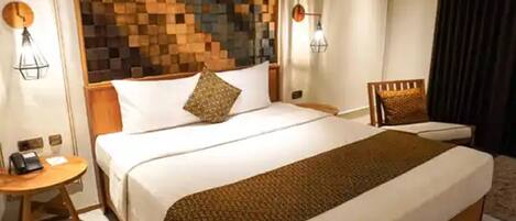A hotel room with a large bed, a bedside table, a chair, and a wall with a geometric pattern.