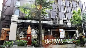 Un edificio con un letrero que dice 'de JAVA HOTEL' y un árbol en primer plano.