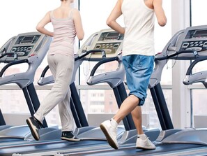 Two people running on treadmills in a gym with large windows and a view of buildings outside. - de Java Hotel Bandung (Bandung)