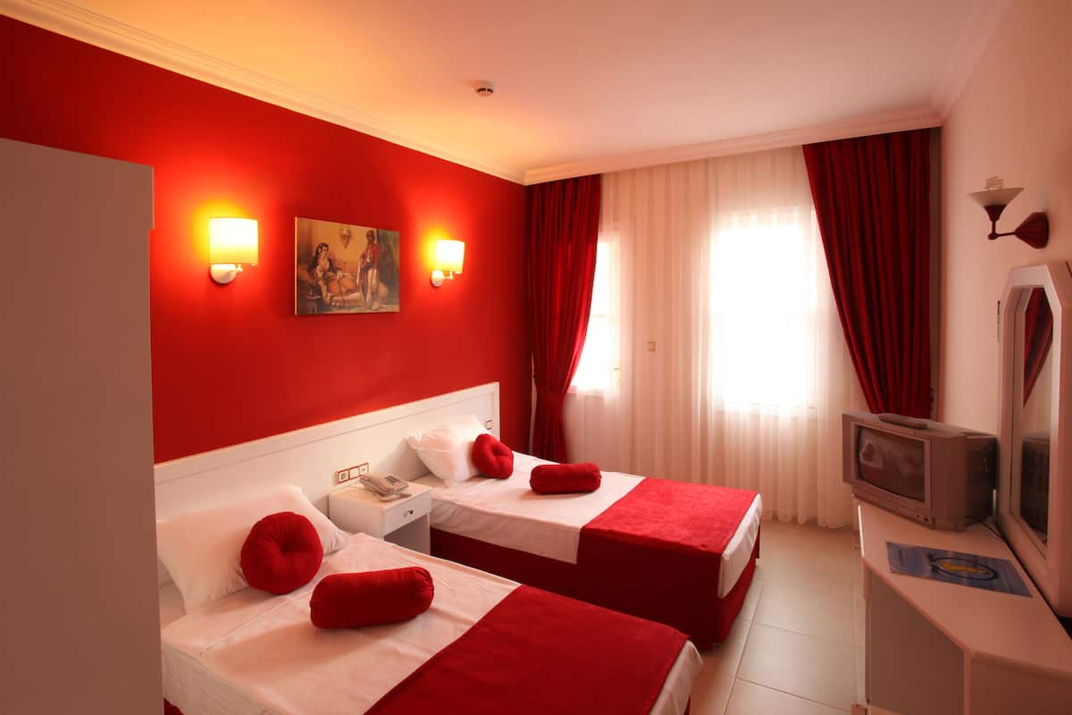 A hotel room with two beds, red bedding, a TV, and two wall-mounted lights.