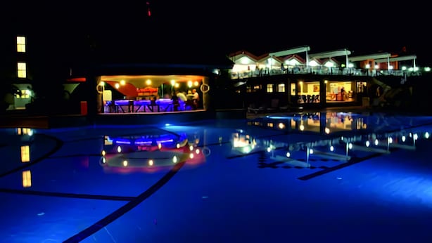A nighttime view of a hotel with a pool reflecting lights, a bar area, and a building with multiple levels and balconies. - Destina Hotel (Fethiye)