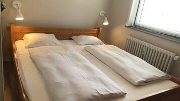 Een tweepersoonsbed met witte lakens, twee bedlampen en een raam met zonwering.