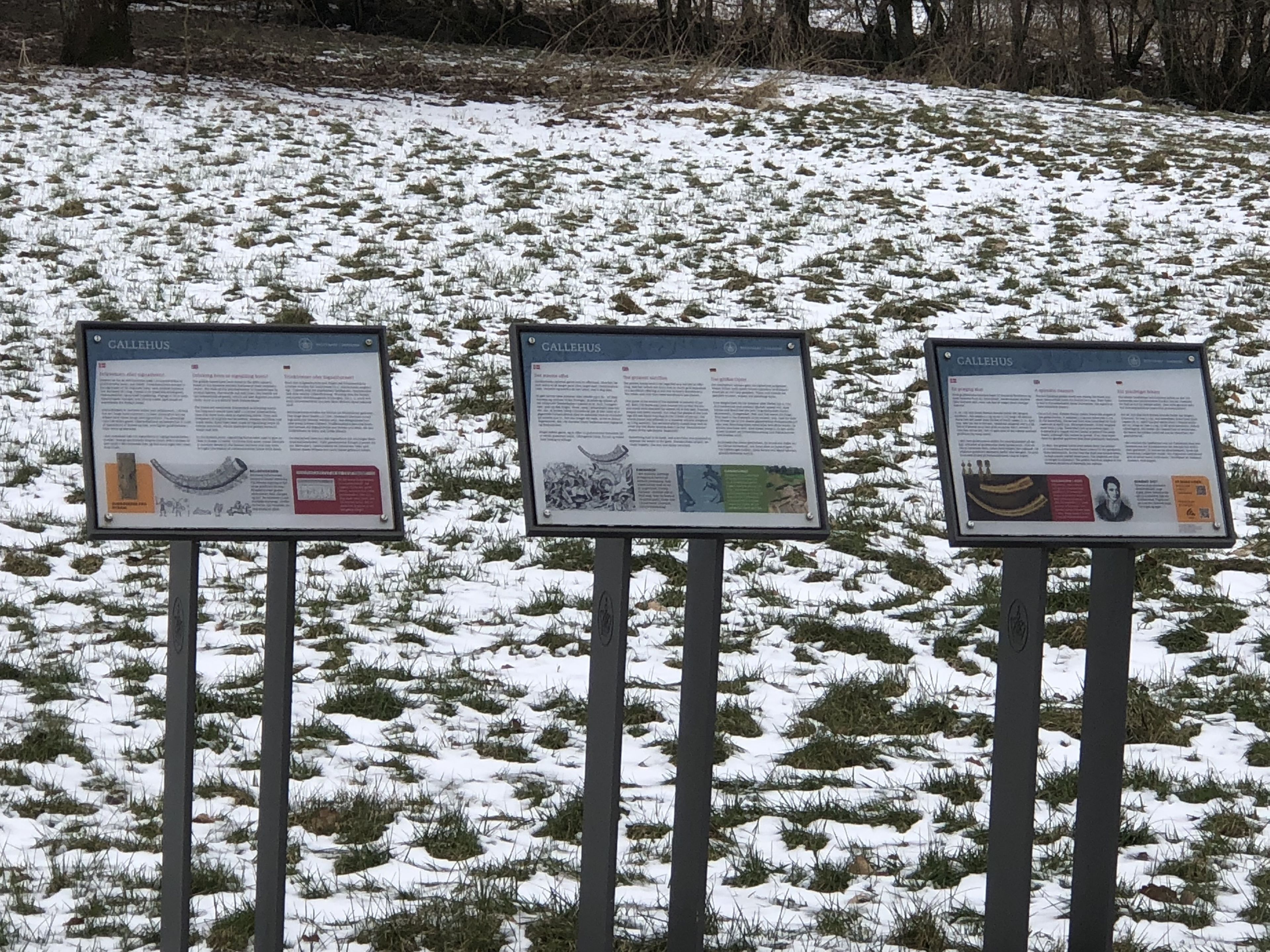 Three informational signs on a snowy field.