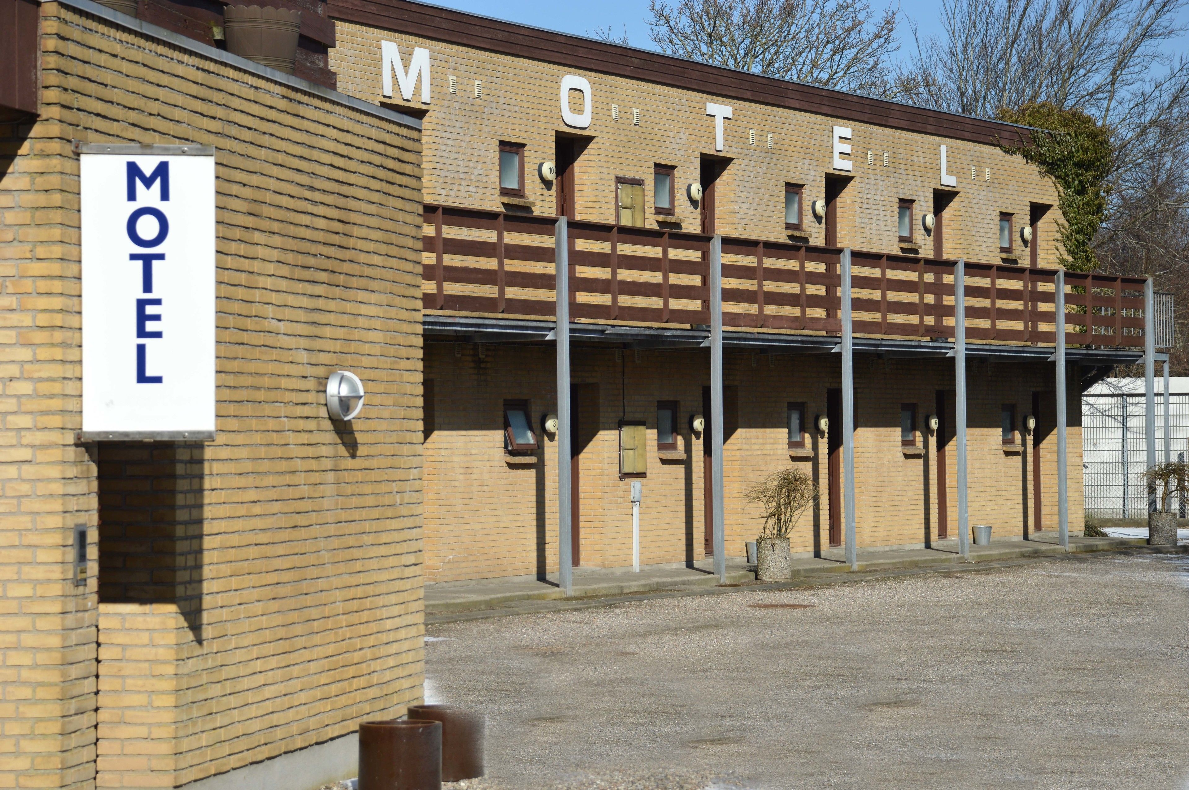 Un motel con un cartel, varias habitaciones y una zona de estacionamiento.