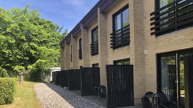 Un bâtiment moderne avec une façade en briques, de grandes fenêtres et un chemin de gravier menant à un patio doté d’un espace salon extérieur.
