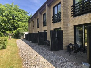 A modern building with a brick facade, large windows, and a gravel pathway leading to a patio area with outdoor seating. - Motel Apartments Tønder (Tonder)