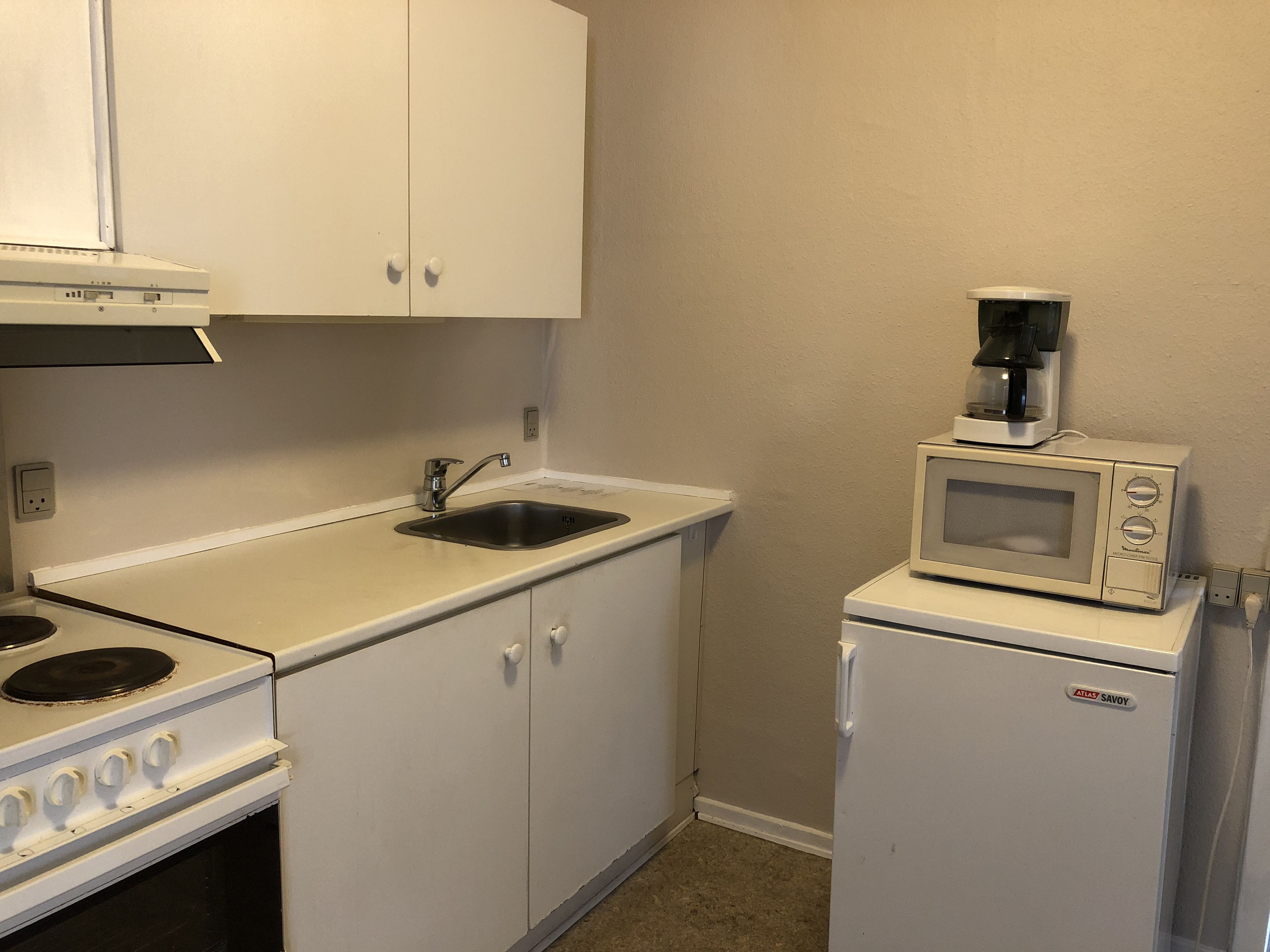 A compact kitchen with white cabinets, a sink, a stove, a microwave, and a refrigerator.