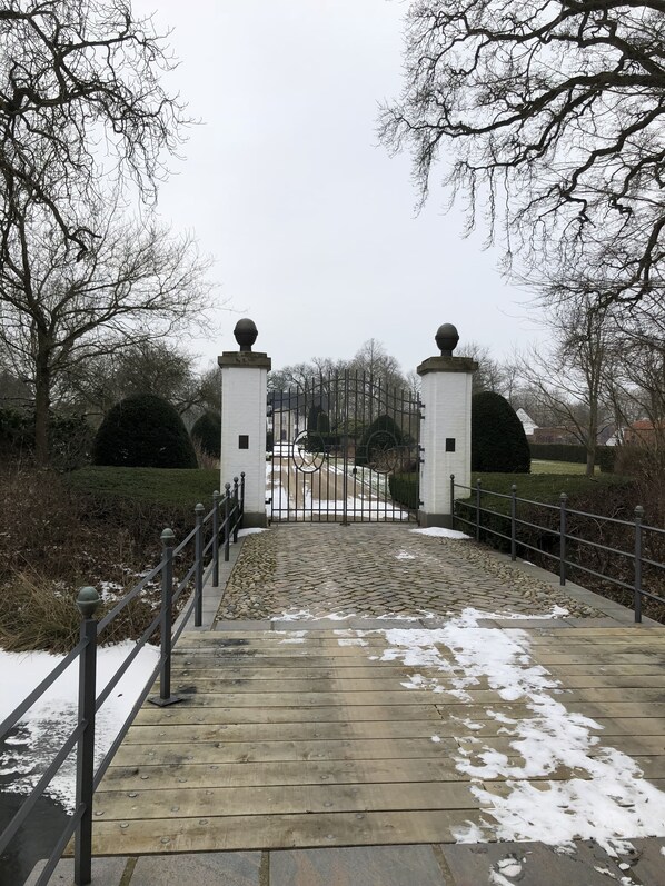 A gated entrance with a cobblestone path leading to a white building with two columns topped with spherical ornaments.