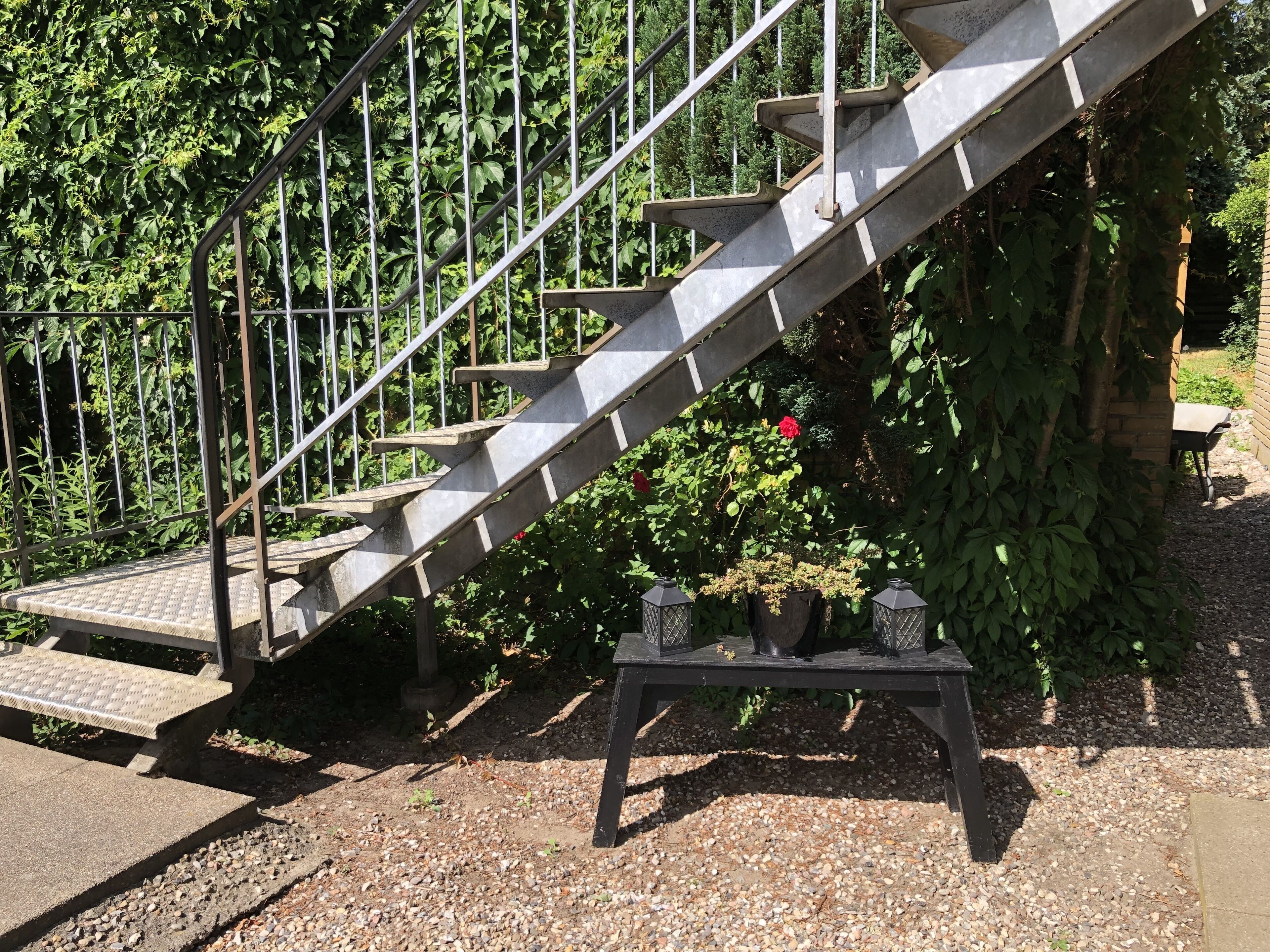 A concrete staircase with metal railings, leading to a garden area with potted plants and a brick wall.