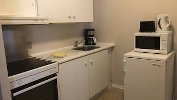 Una cocina compacta con armarios blancos, estufa, microondas y refrigerador.