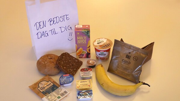 Variedad de alimentos, incluyendo un plátano, pan, un envase de yogur, un tarro de miel y una bolsa de café.