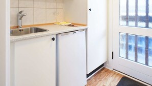 Une cuisine compacte avec des meubles blancs, un évier en acier inoxydable et un lave-vaisselle encastré.