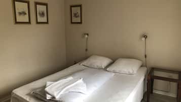A neatly made bed with white linens and pillows, a wooden nightstand with a lamp, and three framed artworks on the wall.