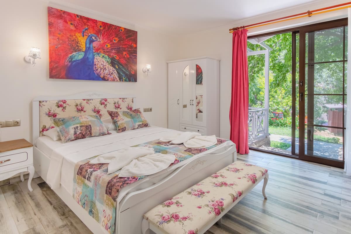 A bedroom with a bed, a bench, a wardrobe, and a peacock painting.