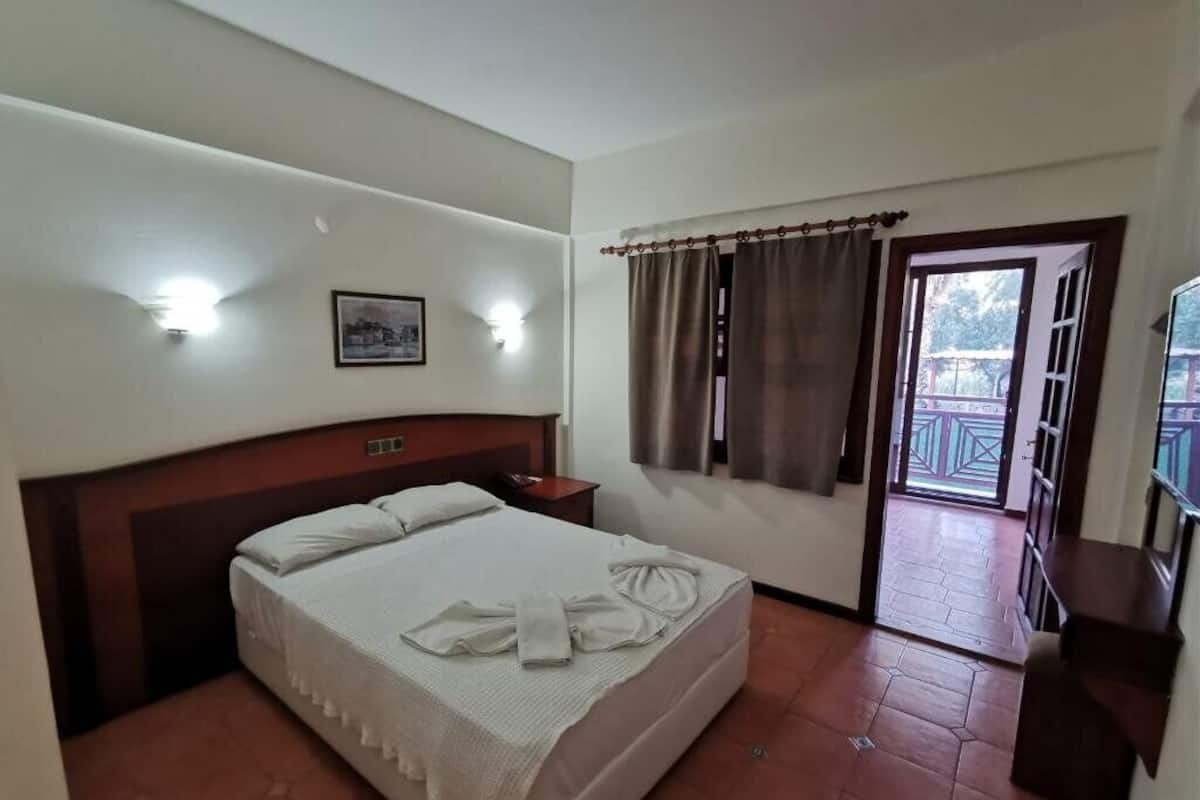 A hotel room with a bed, bedside table, and a view of the outside balcony.