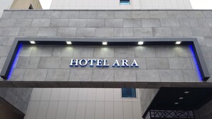 L’entrée de l’HÔTEL ARA se distingue par son design moderne, avec une enseigne bien visible et des bandes lumineuses bleues.