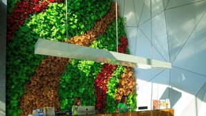 A reception desk with a geometric design, surrounded by a wall of green foliage and red flowers. - Maxone Hotels at Malang (Malang)