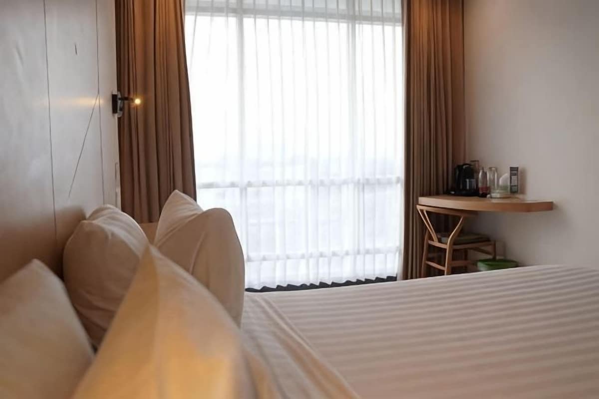 A hotel room with a bed, a desk with a chair, and a window with curtains.