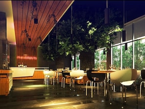 A modern restaurant interior with a wooden ceiling, large windows, and a central tree. Tables and chairs are arranged for dining. - Maxone Hotels at Malang (Malang)