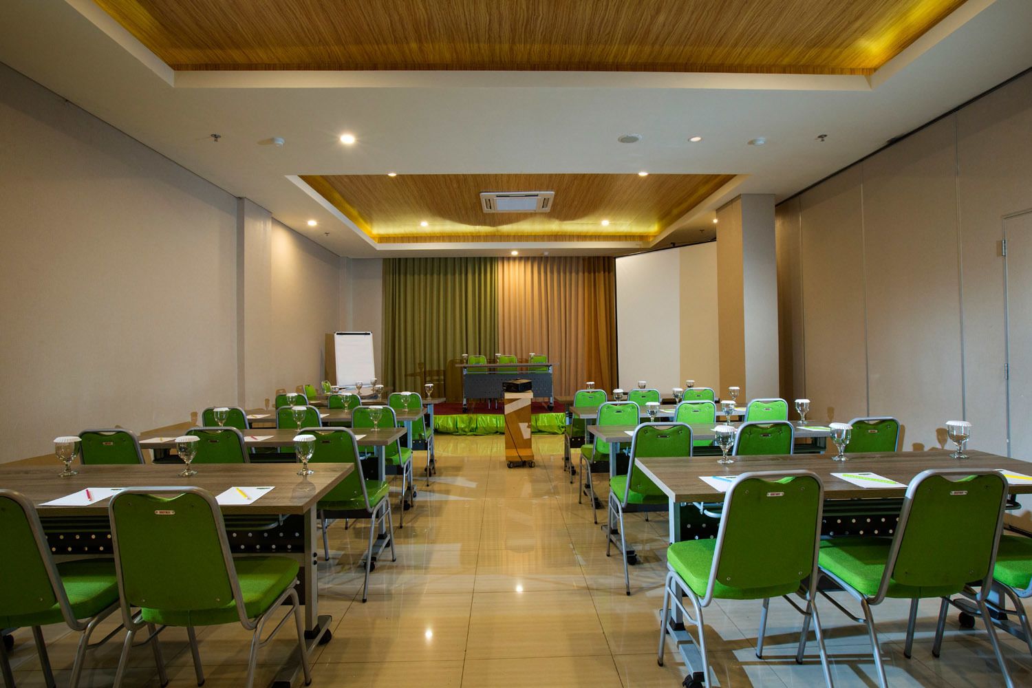 A conference room with green chairs, tables, a podium, and a whiteboard.