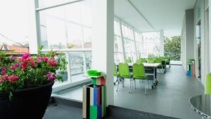 A modern indoor space with large windows, green chairs, and a potted plant with pink flowers. - Maxone Hotels at Malang (Malang)