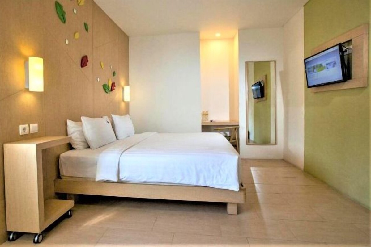 A modern hotel room with a large bed, a bedside table, a TV mounted on the wall, and a wall-mounted light fixture.