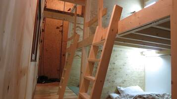 A wooden bunk bed room with a ladder, wooden walls, and a window.