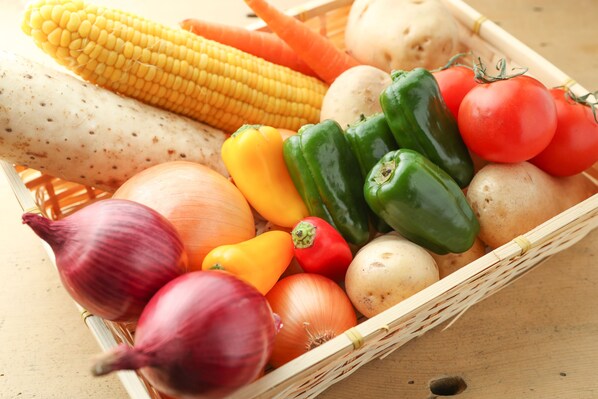 A basket of fresh vegetables including corn, carrots, onions, peppers, and tomatoes. - SappoLodge - Hostel (Sapporo)