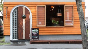 A wooden building with a large arched door, a window with a hanging light, and a signboard with information. - SappoLodge - Hostel (Sapporo)