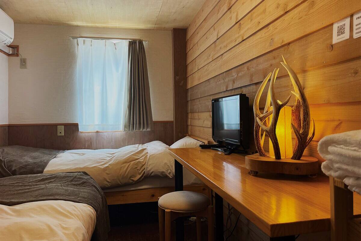 A room with two beds, a desk with a television, and a decorative wooden sculpture.
