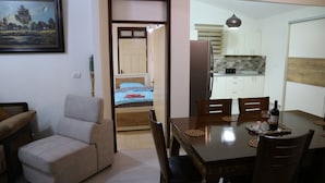 A dining area with a wooden table, chairs, and a bottle of wine. There is a bed with a blue blanket in the background. - Santa Maria Guest House (Haifa)