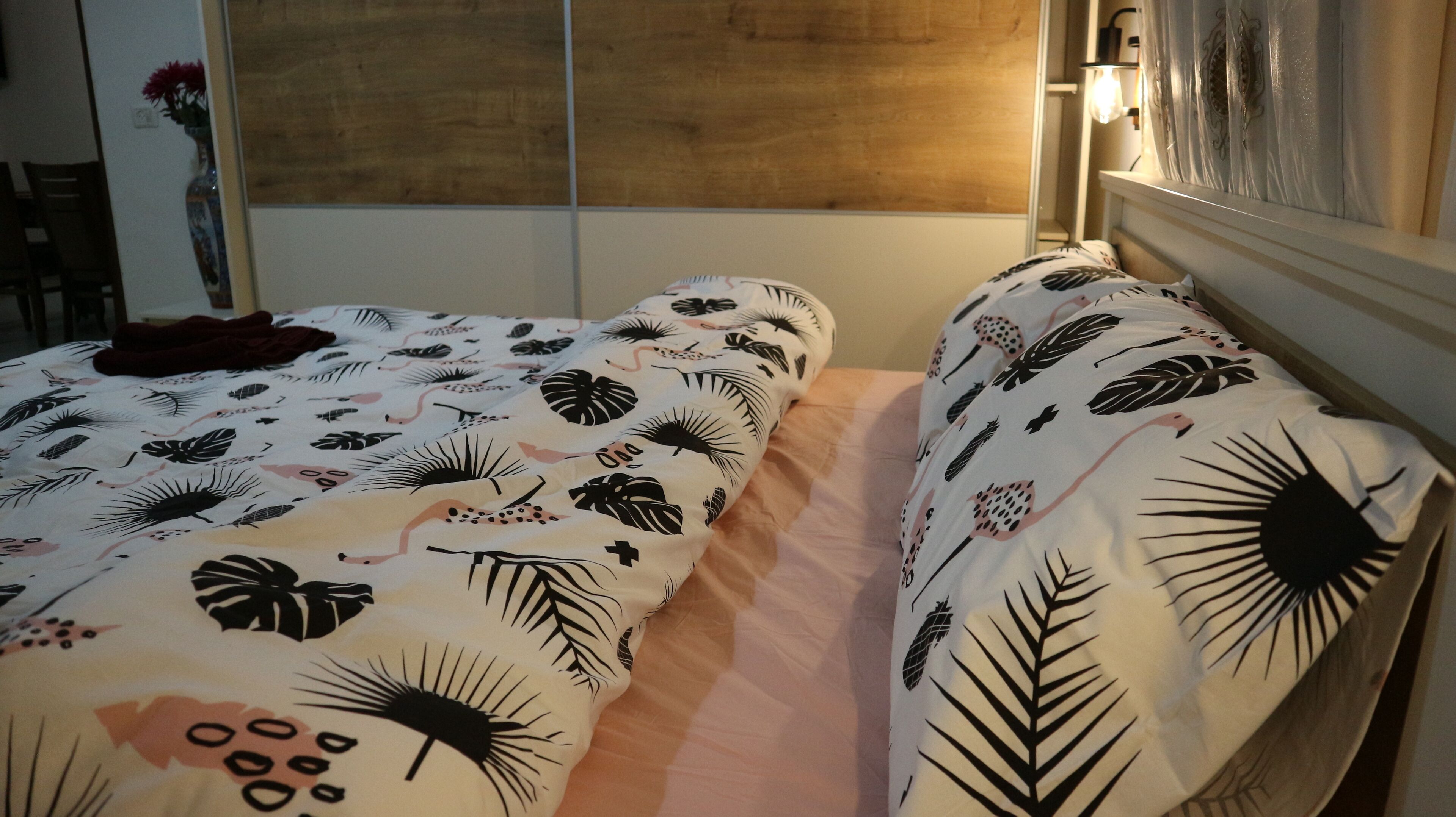 Una habitación con dos camas, cada una con una colcha estampada. Se observa un cabecero de madera en el lado derecho y una pared con un panel decorativo sobre las camas.