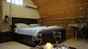 A cozy bedroom with a wooden ceiling, a bed with white linens, a bedside table with a wine glass, and a small table with a candle and decorative items. - Santa Maria Guest House (Haifa)