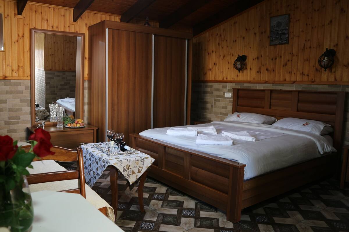 A hotel room with a wooden bed, a nightstand, a mirror, and a table with a vase of red roses.