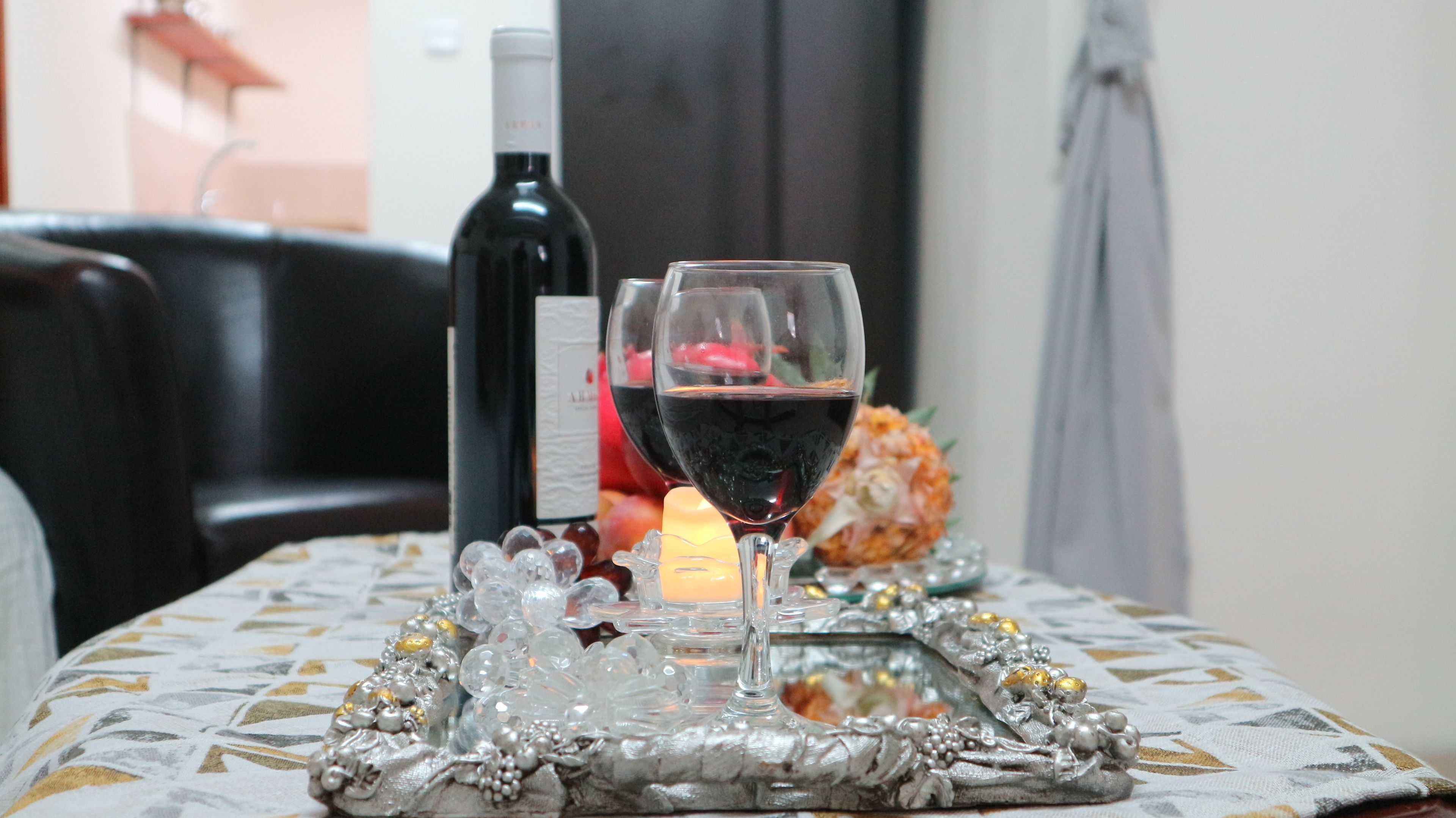 A table with a bottle of red wine, two wine glasses, a candle, and decorative items.