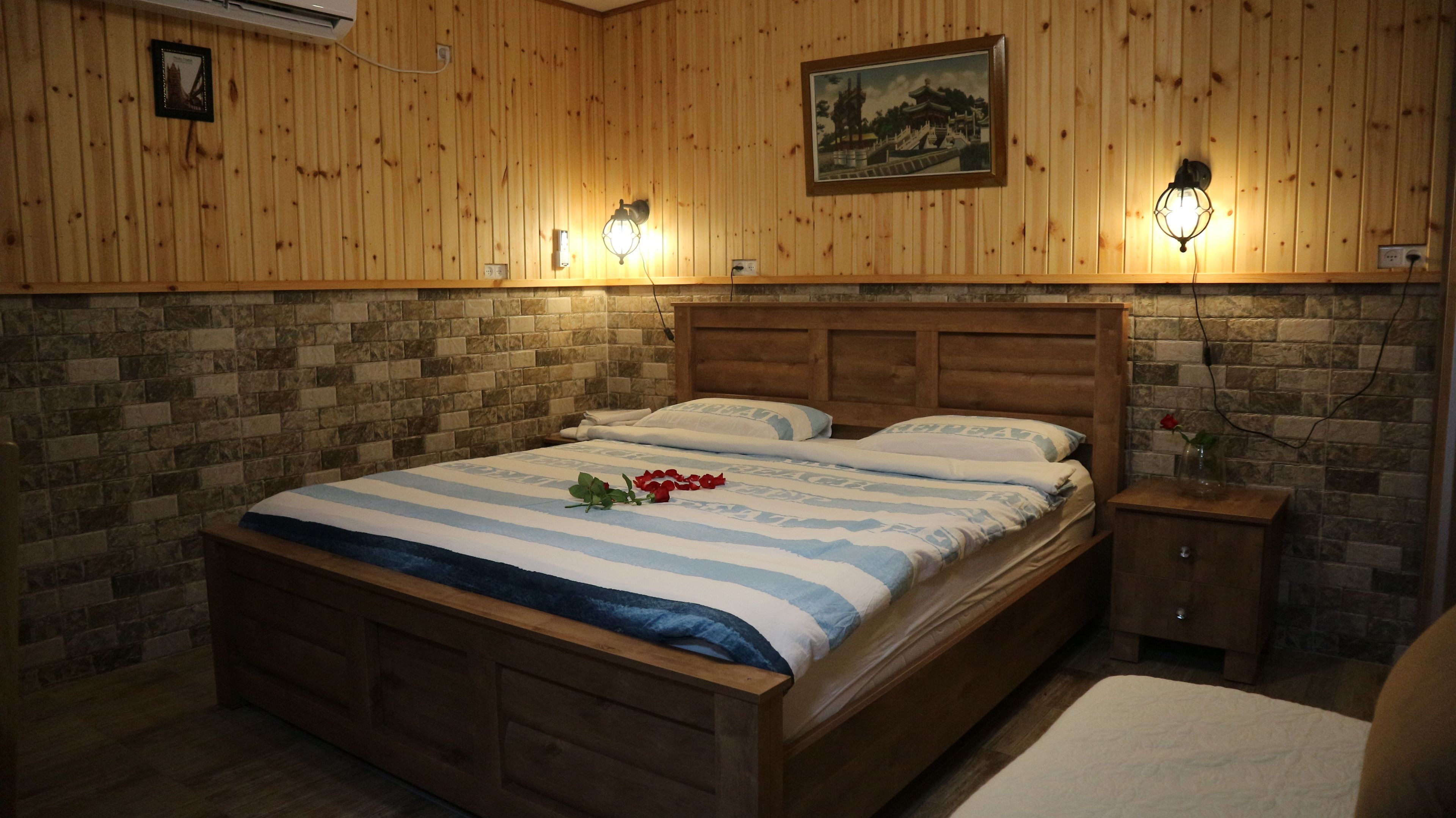 A wooden-paneled bedroom with a bed, nightstands, and a stone wall.